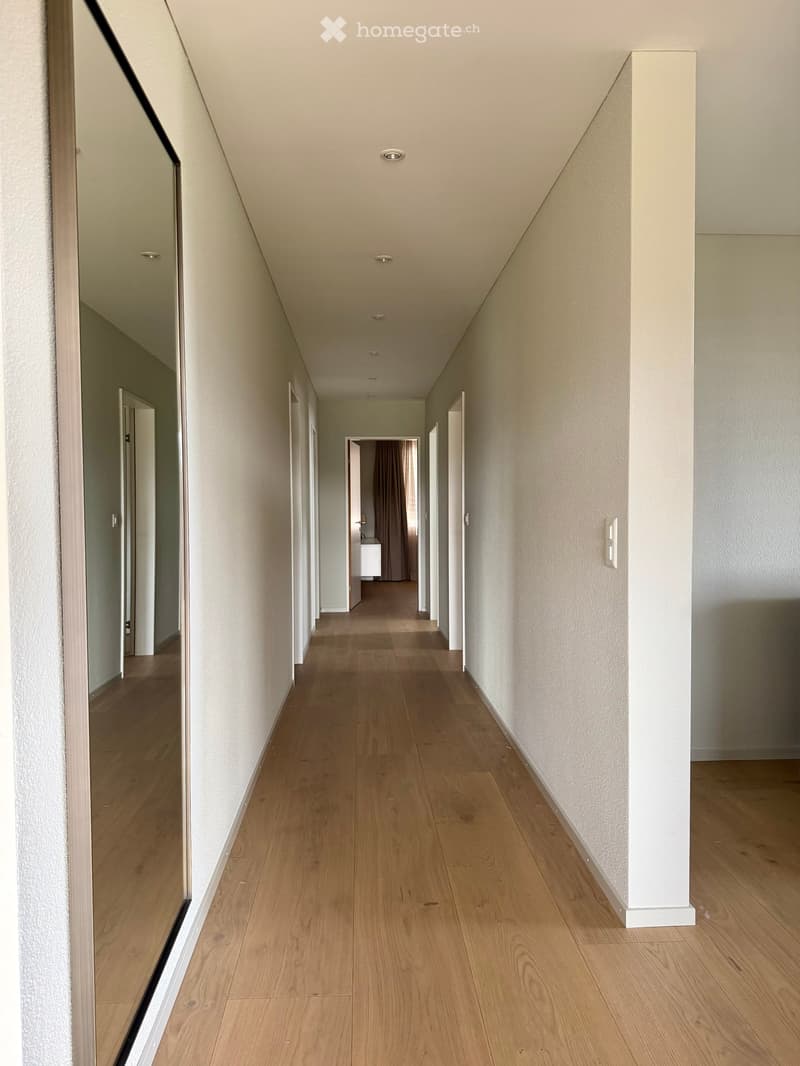 Empty hallway with wooden flooring, white walls, and several doors leading to other rooms.