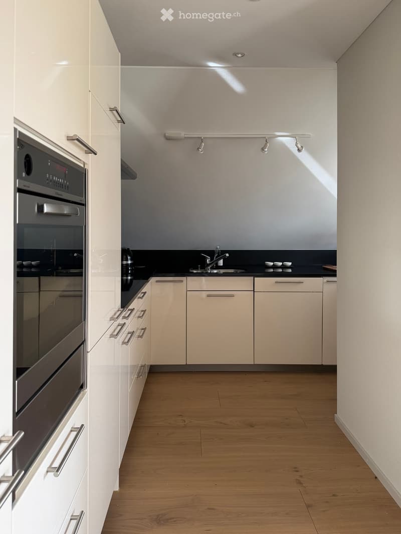 Modern kitchen with white cabinets, wooden flooring, and stainless steel oven and sink.