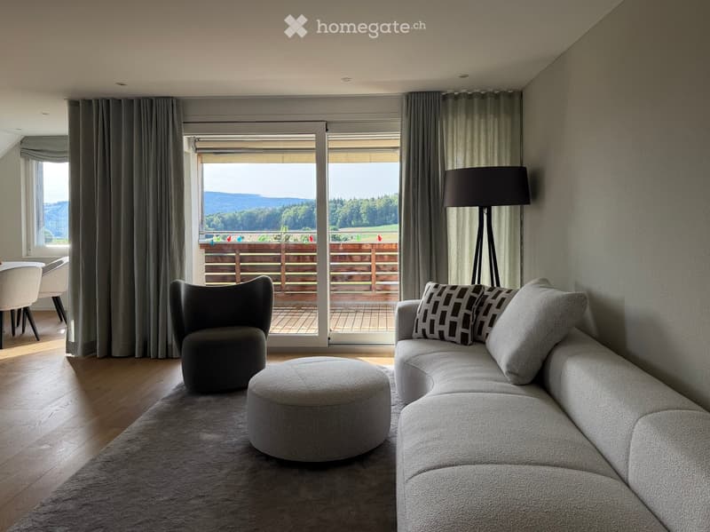 Modern living room with a grey sectional sofa, ottoman, armchair, dining table, and floor lamp, overlooking a scenic outdoor view.