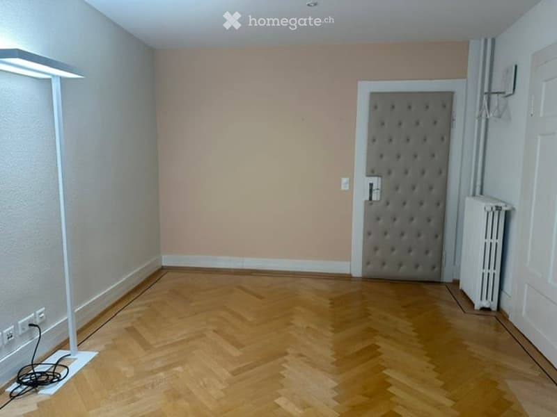 Empty room with wooden herringbone flooring, light-colored walls, a radiator, and a door with a textured panel.