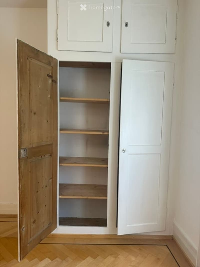 Empty pantry with wooden shelves and white cabinetry, no items stored inside.