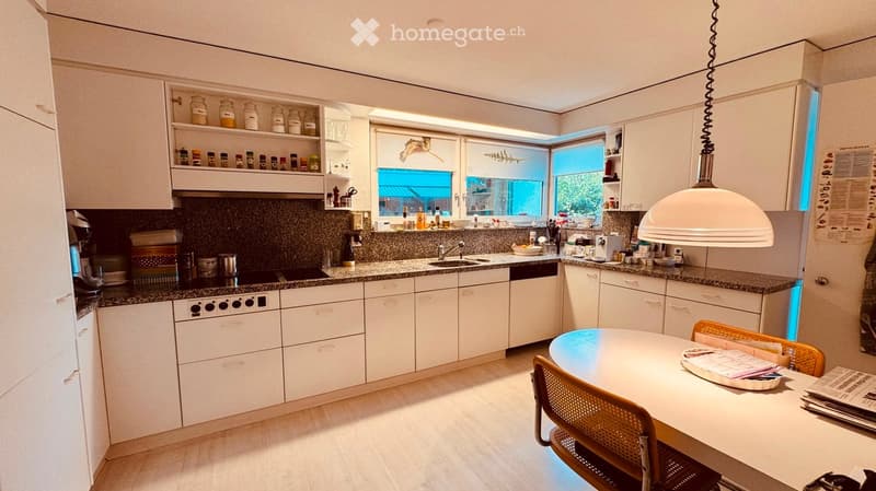 Modern kitchen with white cabinets, granite countertops, built-in appliances, and a round dining table with chairs.