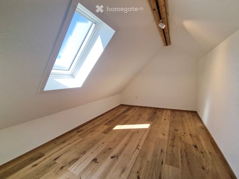 Empty attic space with wooden flooring and a skylight window, featuring white walls and a slanted ceiling.