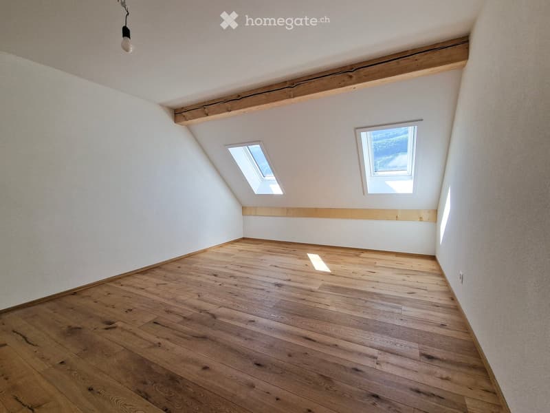 Empty attic room with wooden flooring, white walls, exposed wooden beams, and skylight windows.