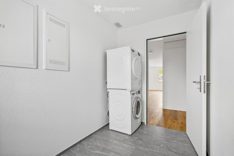 Empty room with a white washing machine, dryer and two wall mounted electrical boxes