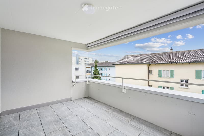 Balcony with railings, gray tile flooring, open window, sky view.
