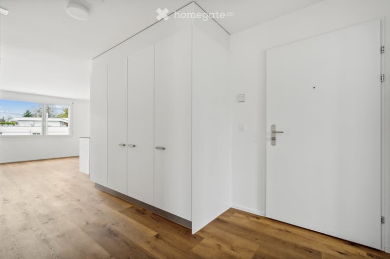 Empty room with white wardrobes, wooden floor, and a window