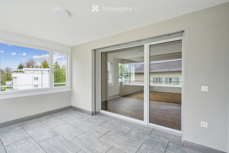Empty room with tiled floor, large windows, and sliding glass doors leading to a wooden deck area.