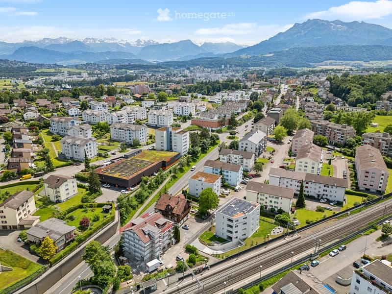 Aerial view of a residential area with multiple apartment buildings, surrounded by green spaces and a scenic mountain backdrop.