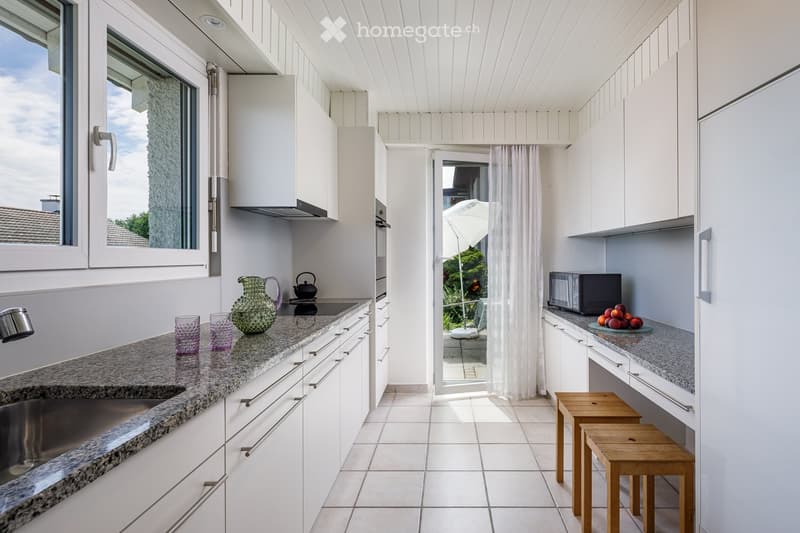 Modern kitchen with white cabinets, granite countertops, and a window overlooking a balcony. Includes a sink, oven, microwave, and decorative items on the counter.
