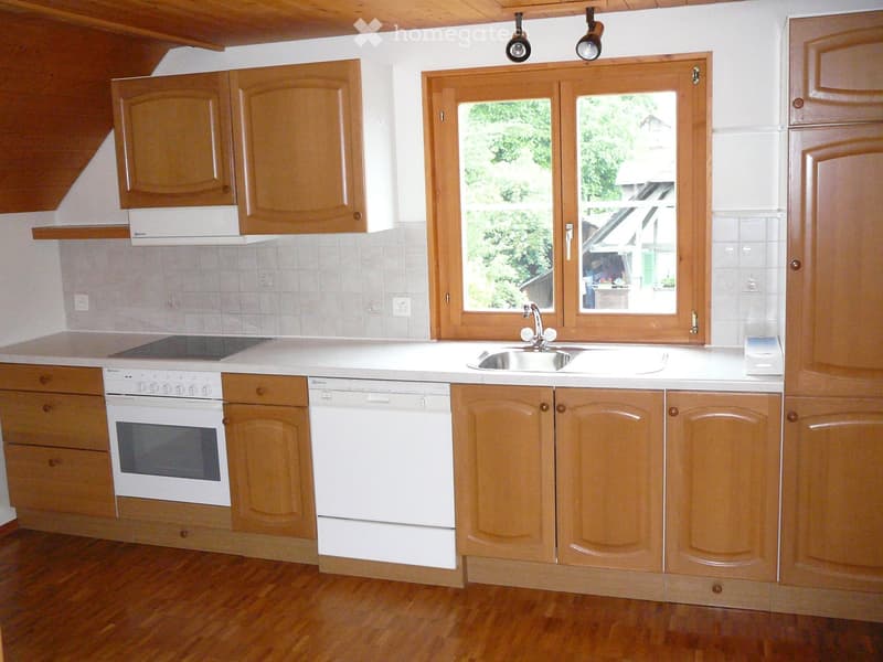 Modern kitchen with wooden cabinets, white appliances, and a large window overlooking a garden.