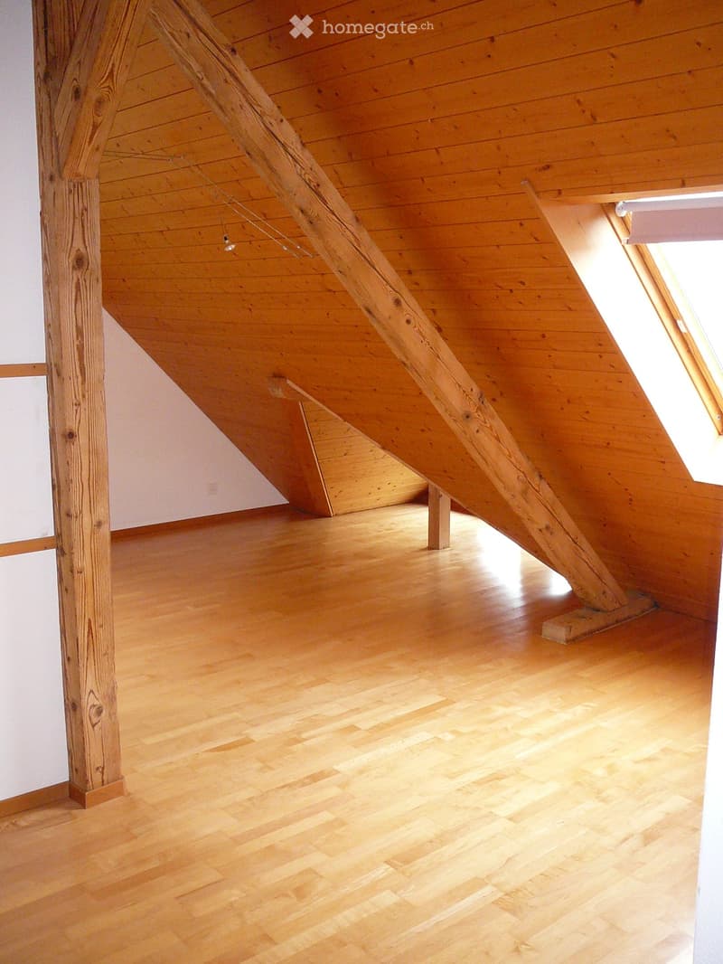 An empty attic space with wooden floors and exposed wooden beams, featuring a skylight window allowing natural light to enter.