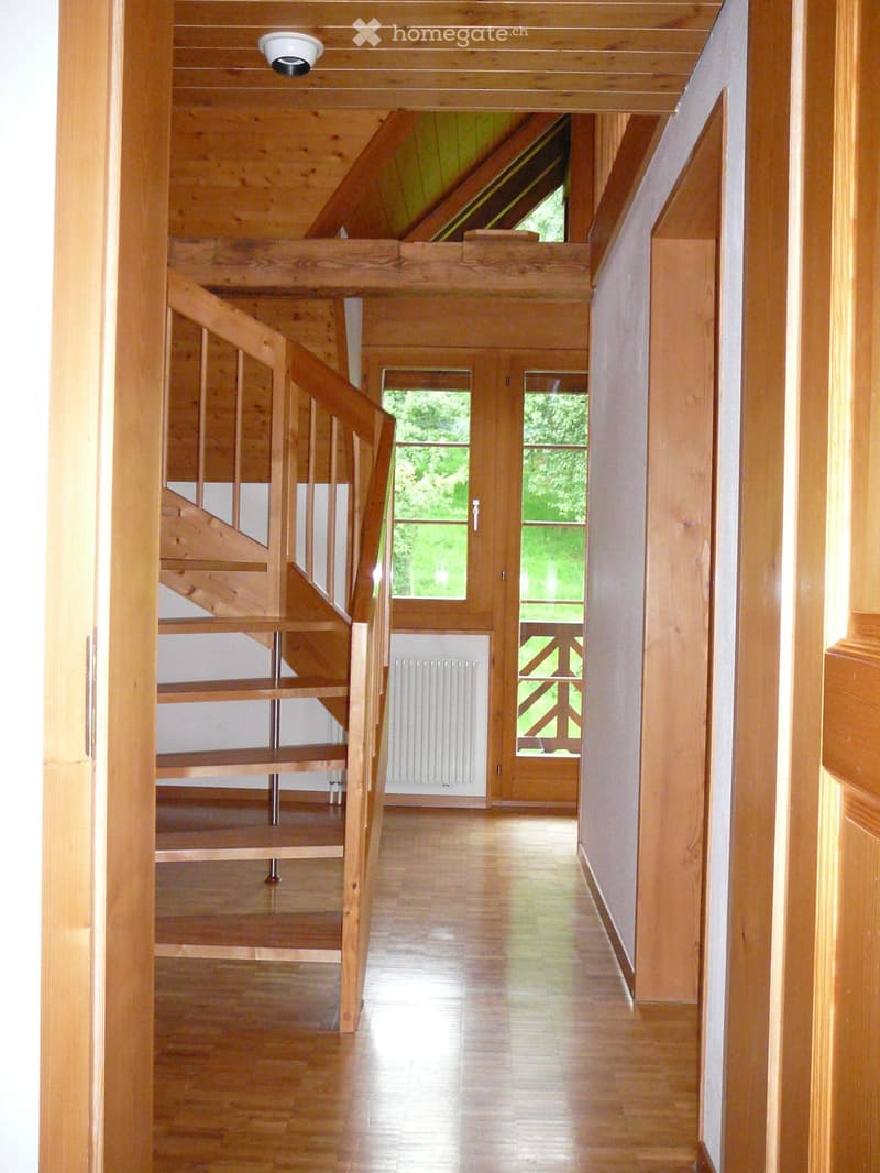 Bright, wooden hallway with polished floor, staircase leading upwards, and large windows letting in natural light.