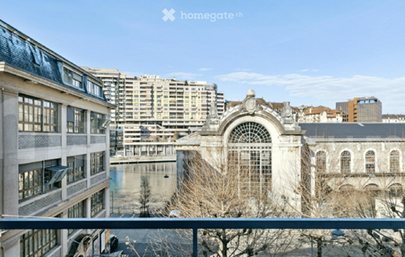 Balcony overlooking a cityscape with modern and historic buildings, a canal, and a clear blue sky.