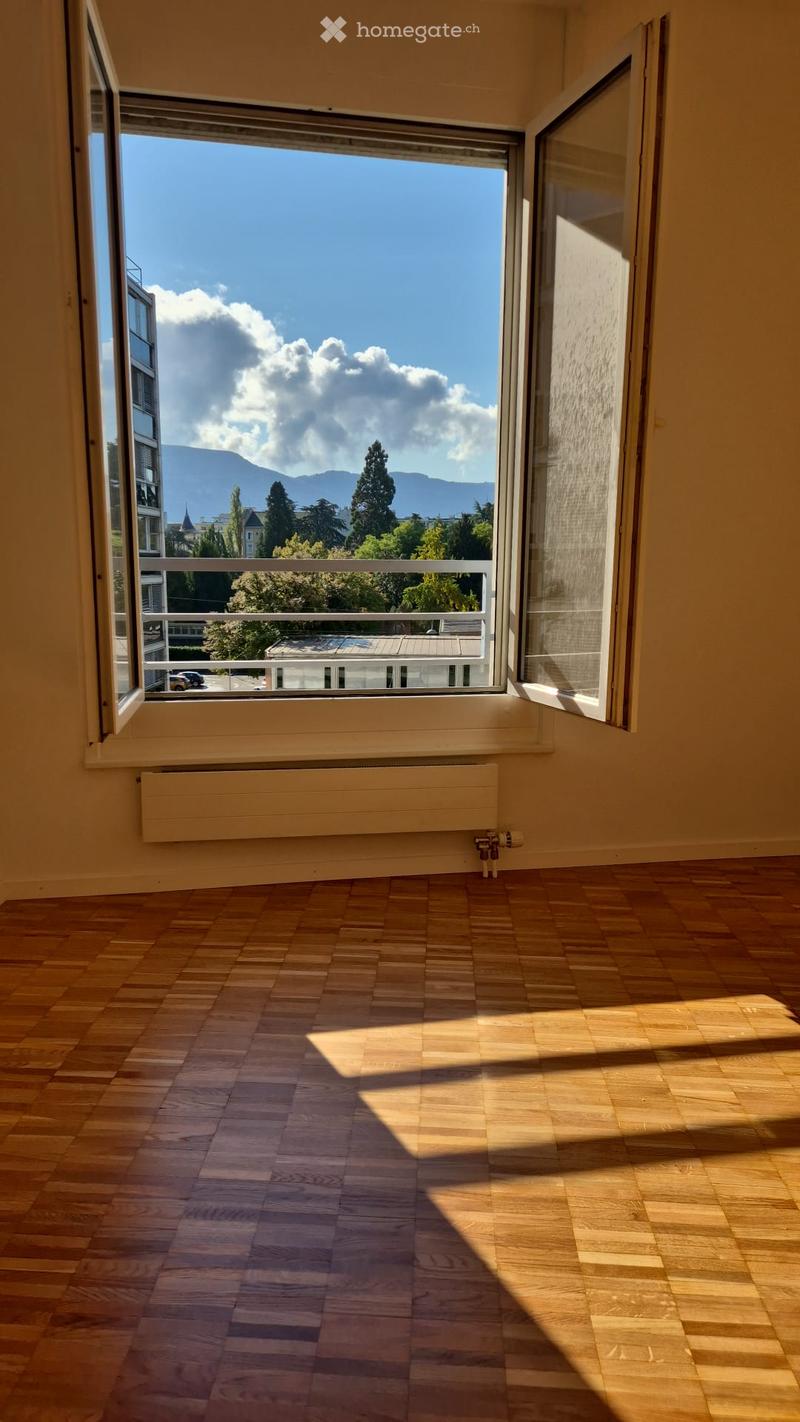 Empty room with wooden flooring, large window offering a scenic view of mountains and cityscape.