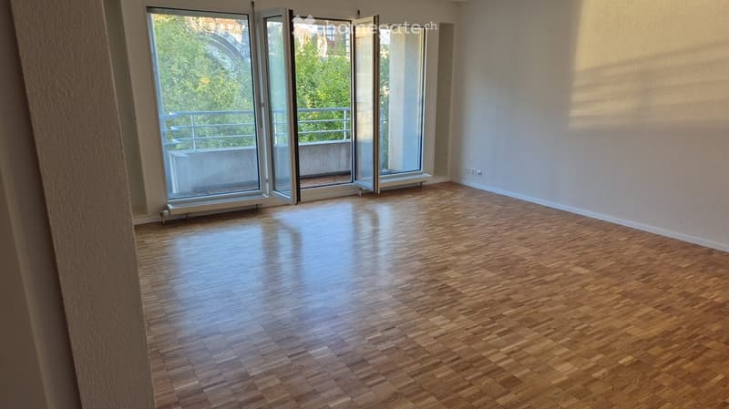 Empty room with wooden flooring, large glass doors leading to a balcony, and white walls.