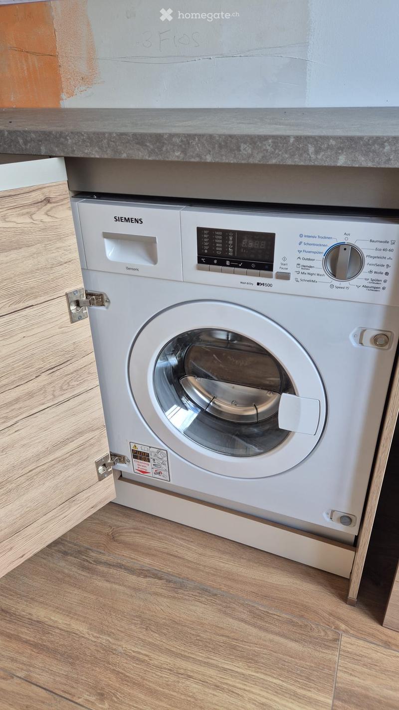 A white Siemens washing machine is installed under a wooden countertop in a bathroom with wooden flooring.