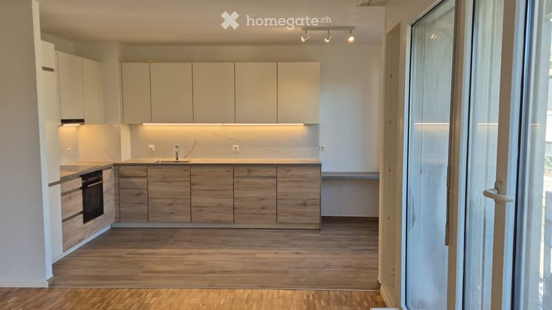 Modern kitchen with light-colored cabinets, wooden lower cabinets, and a sleek countertop. Features an integrated sink and oven, with recessed lighting above the workspace.