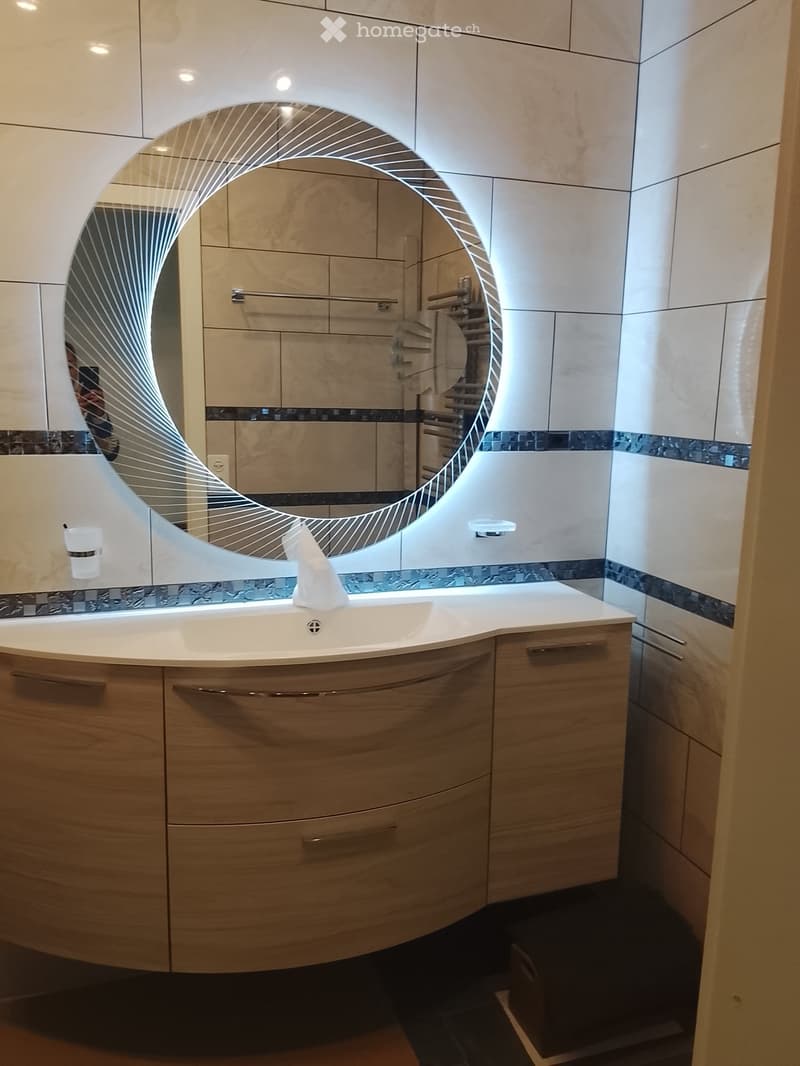 Modern bathroom with a white sink, wooden cabinet, large curved mirror, and a towel on the counter.