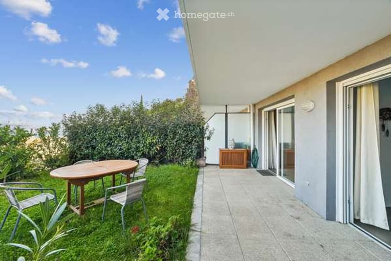 Balcony with a small grassy area, a wooden dining table with four chairs, and a small wooden cabinet with a vase on top.