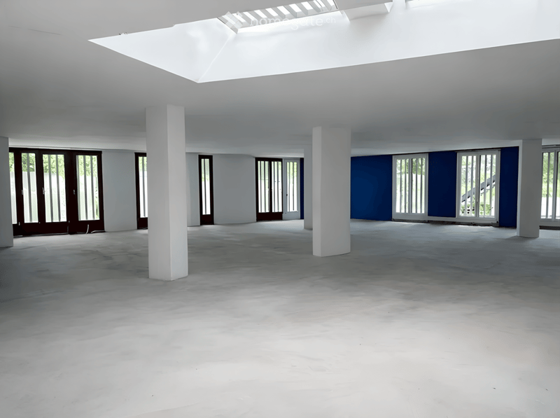 Empty room with white walls, concrete floor, large windows, and white columns. No furniture or equipment present.