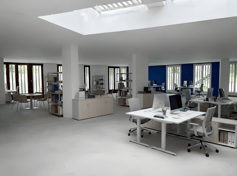 Modern office space with white desks, ergonomic chairs, multiple computer setups, shelves, and cabinets.