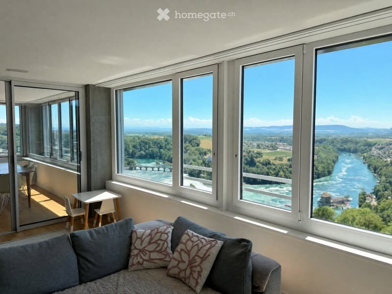 Bright living room with large windows offering scenic views, featuring a sofa, small table, and chairs.