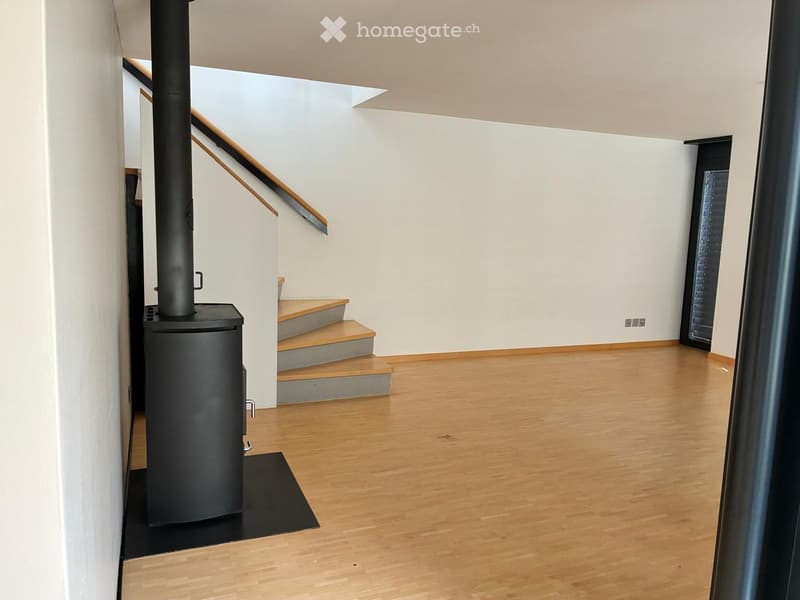 Modern hallway with wooden flooring, white walls, staircase leading upwards, and a black wood-burning stove on the left side.
