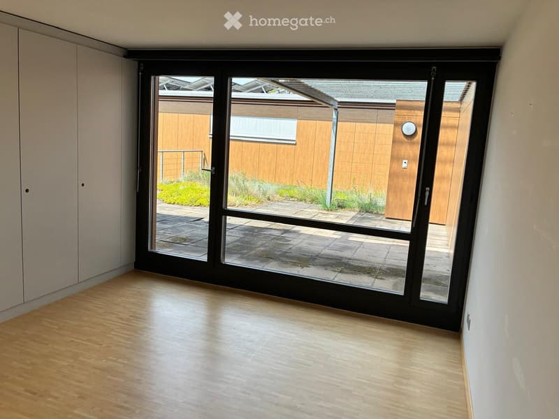 Empty room with wooden flooring and large sliding glass doors leading to an outdoor patio area.