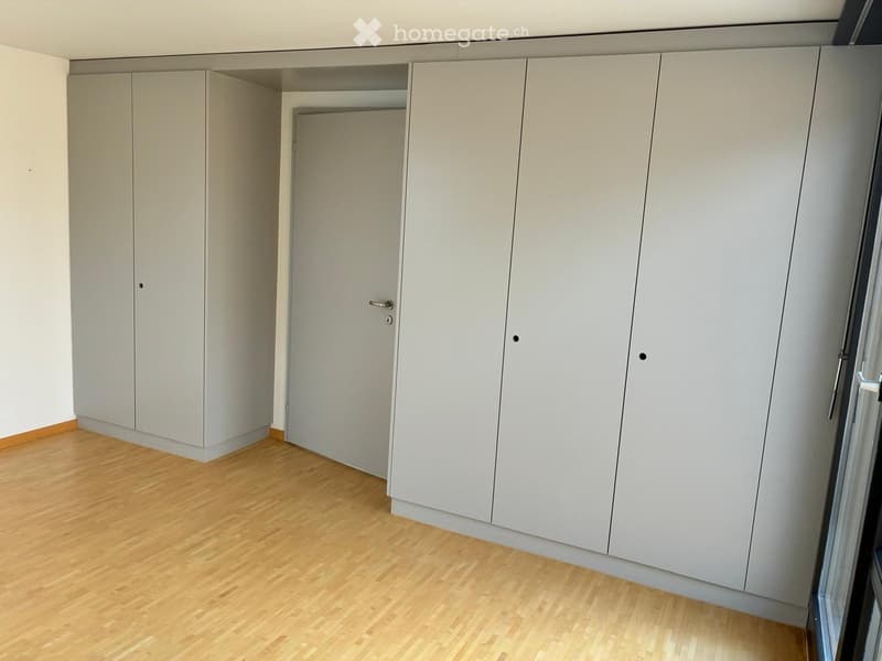 Empty room with light grey built-in wardrobes, wooden flooring, and white walls.