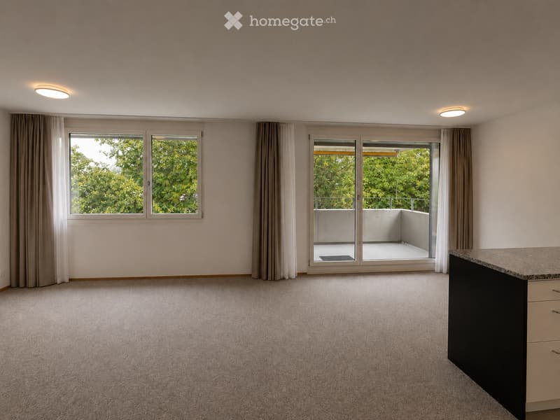 Empty room with carpeted floor, large windows, sliding glass door leading to balcony, and built-in cabinetry.