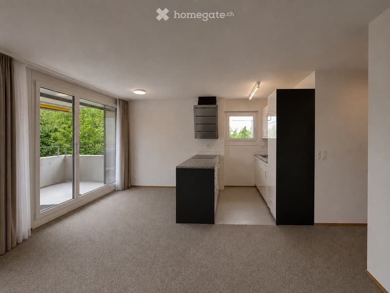 Empty kitchen with modern cabinetry, a countertop, and a large window with a view of greenery. The space features a carpeted floor and recessed lighting.
