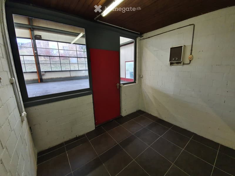 Empty room with white brick walls, dark tiled floor, large windows, and a red door.