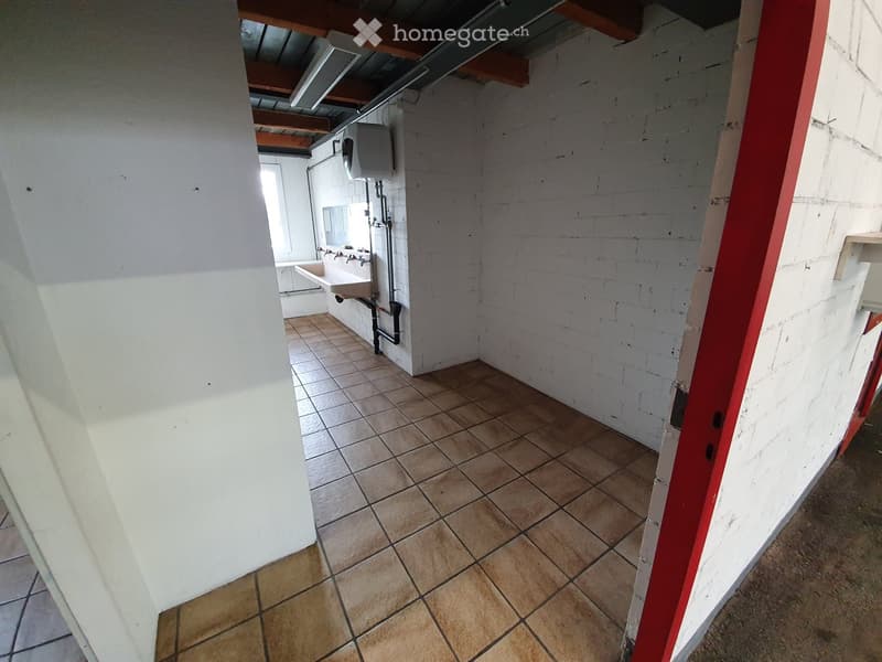 Empty room with tiled floor and white brick walls, featuring a sink and exposed pipes in the background.