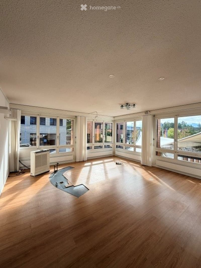 Completely empty room with wooden flooring, large windows, and a radiator. No furniture or equipment.