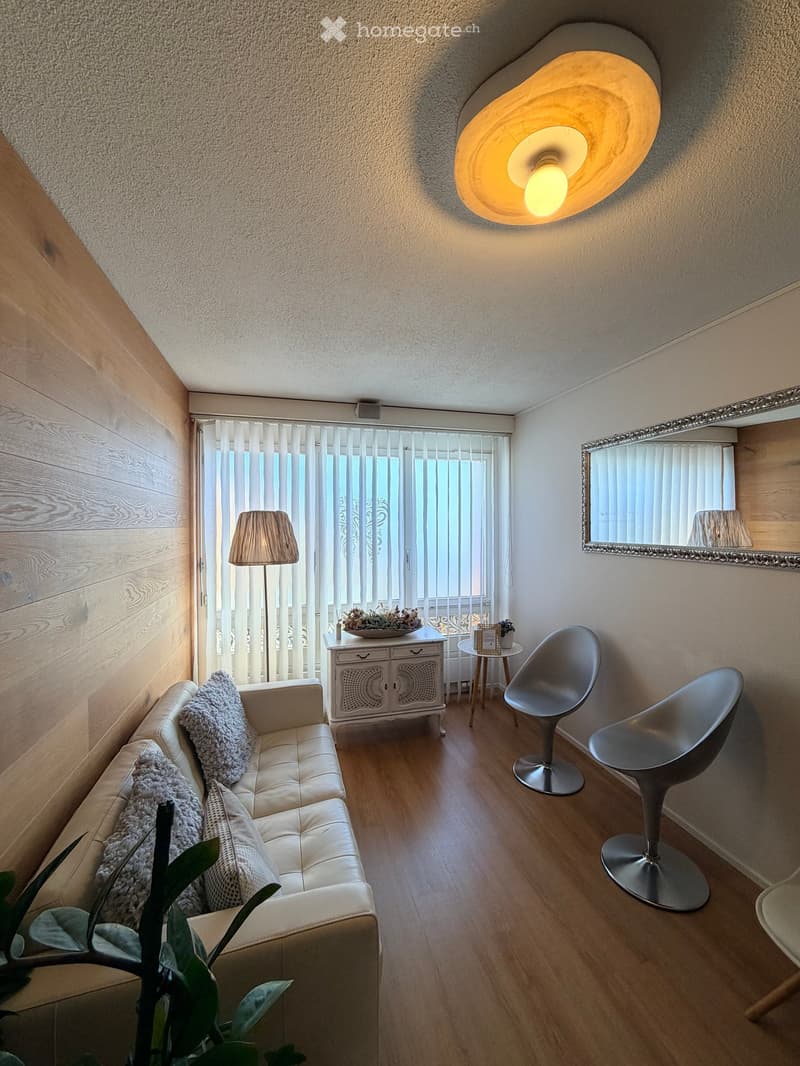Modern living room with a white leather sofa, two modern chairs, a small table, a floor lamp, a wall-mounted lamp, and a decorative mirror.