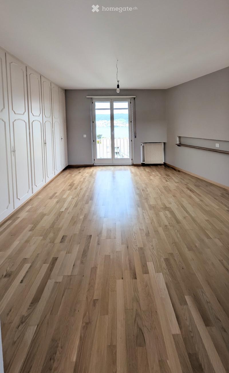 Empty room with wooden flooring, white walls, and a large sliding glass door leading to a balcony with a scenic view.