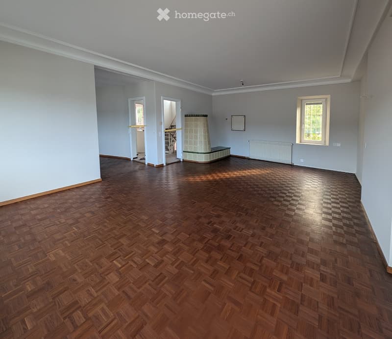 Empty room with wooden herringbone flooring, light grey walls, and a fireplace in the corner. Two doors lead to other areas, and there is a window on the right side.