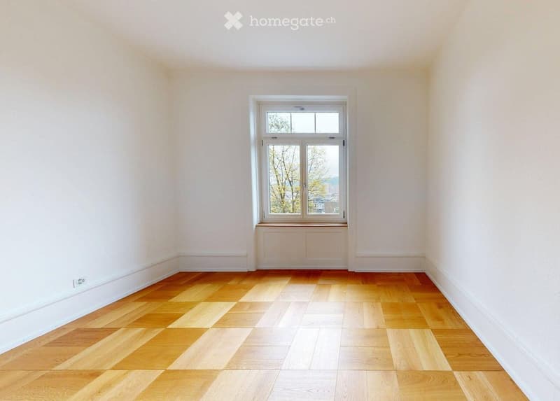 Empty room with light-colored wooden flooring and white walls, featuring a large window with double panes and a radiator below it.