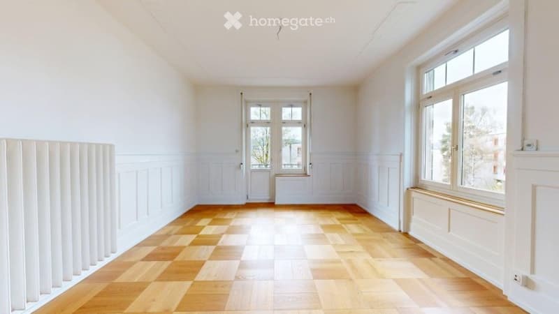 Empty room with wooden flooring, white walls, large windows, and radiators.