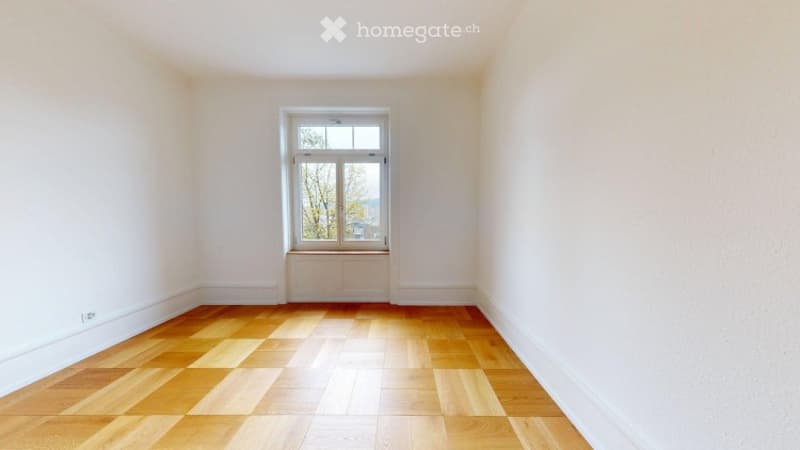 Empty room with wooden flooring and white walls, featuring a single window with a radiator below it.