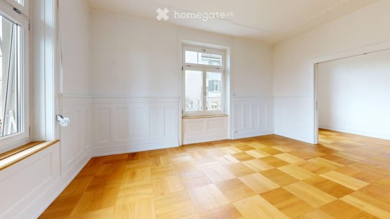 Empty room with wooden flooring, white walls, and large windows. No furniture or equipment present.