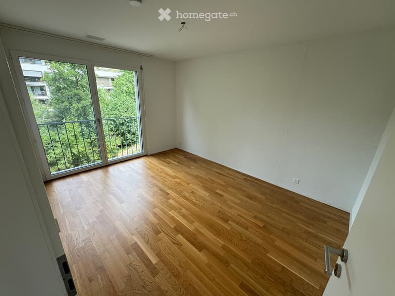 Empty room with wooden flooring, white walls, and large sliding glass door leading to a balcony with a metal railing.