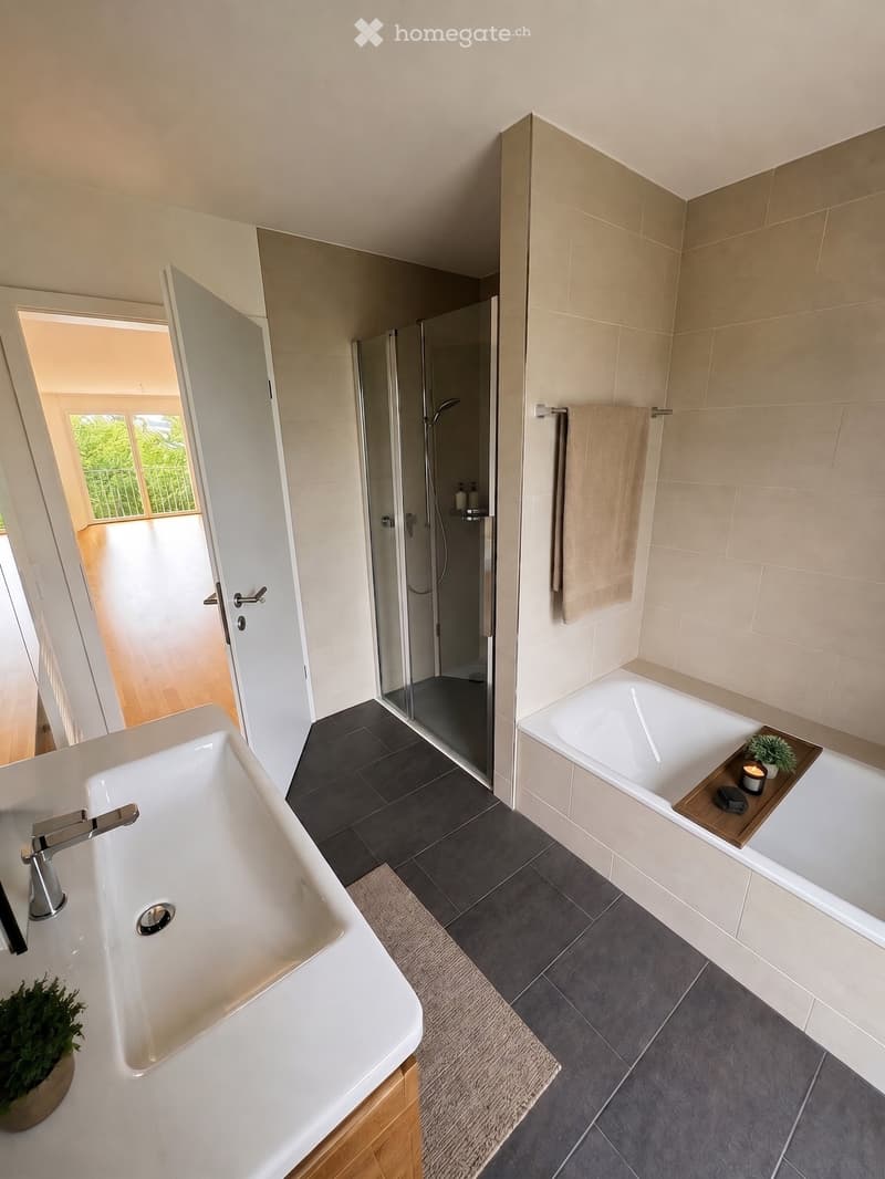Modern bathroom with a bathtub, sink, shower, towel, and decorative items including a candle and small plant.