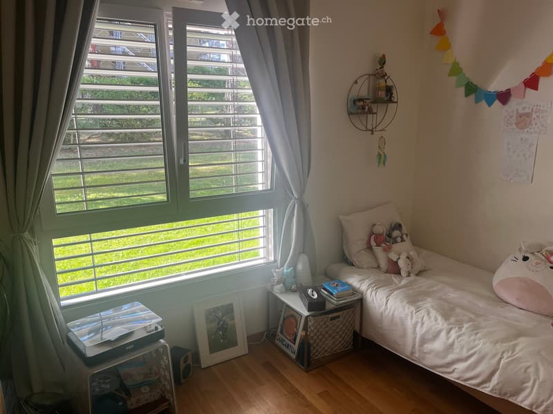 A cozy, well-lit bedroom with a single bed, nightstand, and various decorative items including toys, books, and artwork.