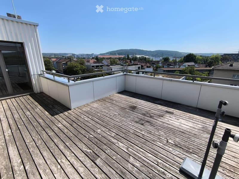 Wooden deck with white railing, overlooking a cityscape with houses and trees.