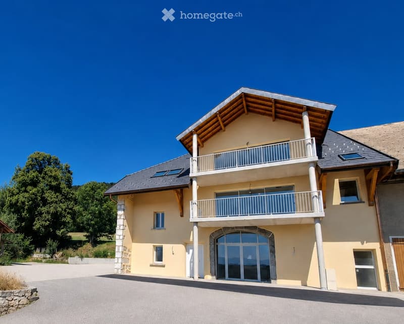 Two-story house with a modern design, featuring a balcony on the upper level, large windows, and a stone foundation.