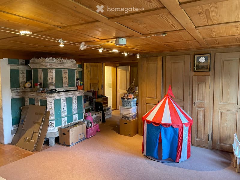 A spacious, well-lit room with wooden ceilings and walls, featuring a colorful children's tent, storage bins, and a vintage toy cabinet.