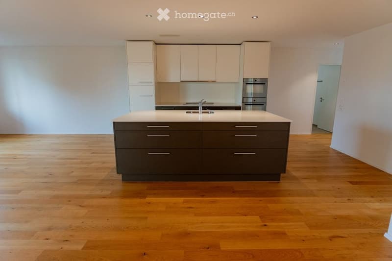 Modern kitchen with light-colored cabinets, a dark kitchen island, and a stainless steel oven. The floor is made of light wood.