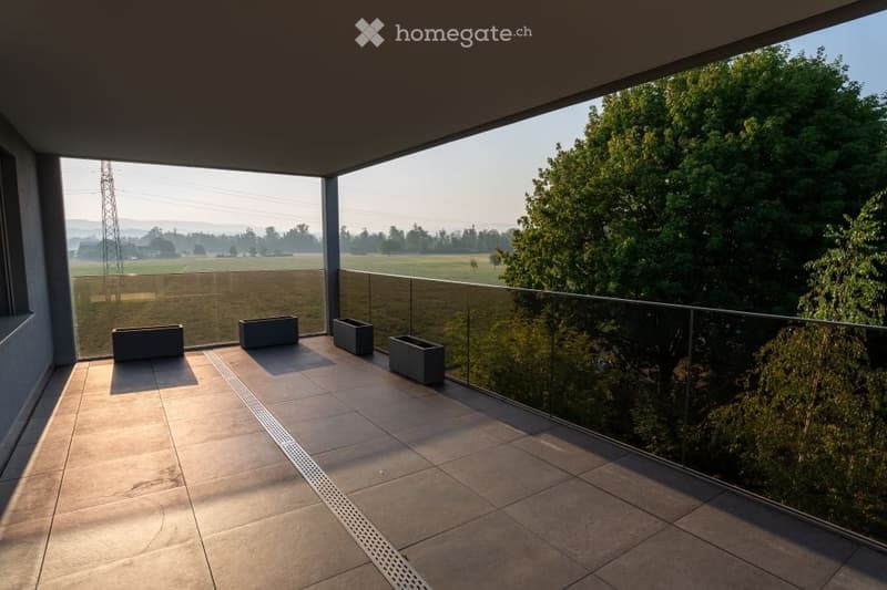 Modern balcony with tiled floor, glass railing, and scenic countryside view.